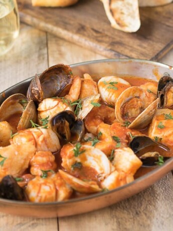 An oval baking dish filled with seafood and shellfish in a tomato broth