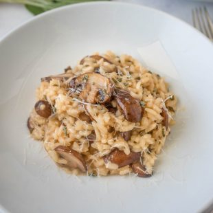 Brown butter mushroom sage risotto topped with grated Parmesan in a white bowl with 3 forks