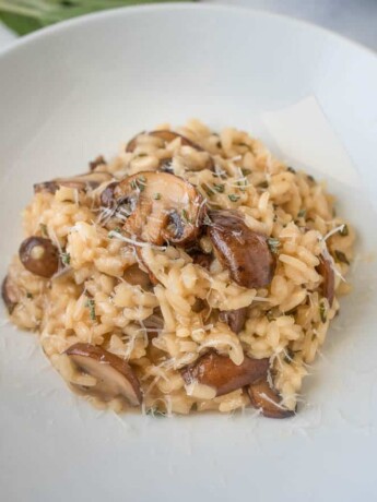 Brown butter mushroom sage risotto topped with grated Parmesan in a white bowl with 3 forks