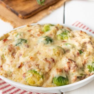 A white oval baking dish filled with Brussels sprouts and bacon cheese sauce