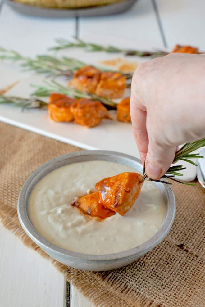 Dipping a buffalo rosemary chicken skewer into blue cheese sauce