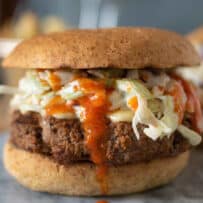 A side view of a buffalo sauce burger, topped with blue cheese celery slaw