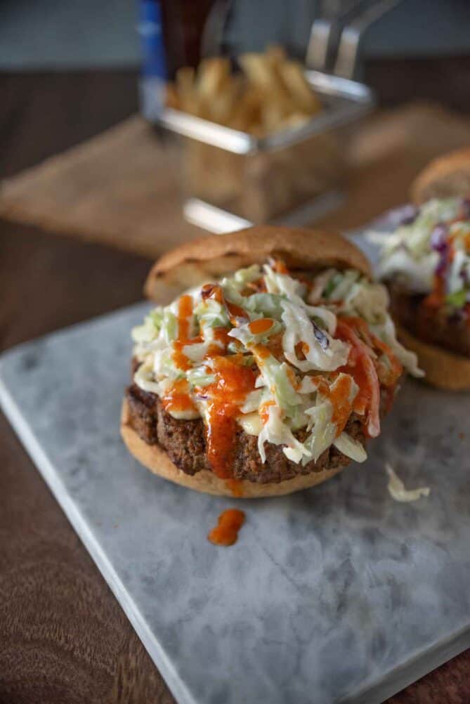 Blue cheese coleslaw piled high on top of a burger, drizzled with buffalo sauce