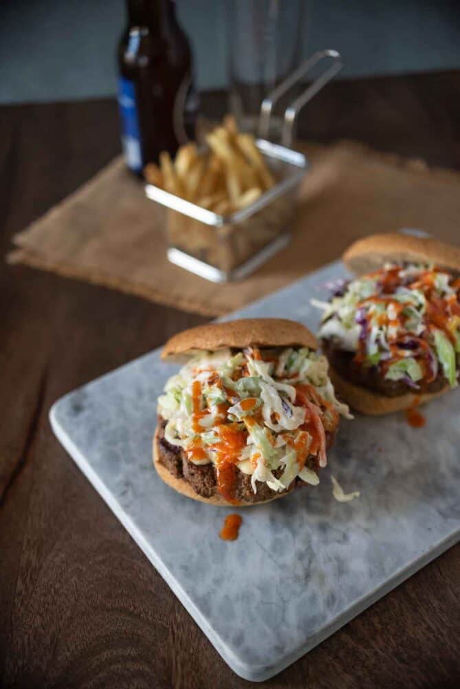 2 buffalo sauce burgers with bun tops off showing the coleslaw on top