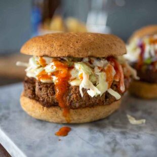 A beef burger in a bun with coleslaw and buffalo sauce