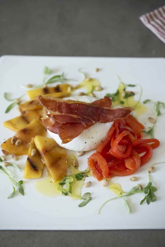 Burrata with charred peaches, red pepper and crispy prosciutto served on a square platter
