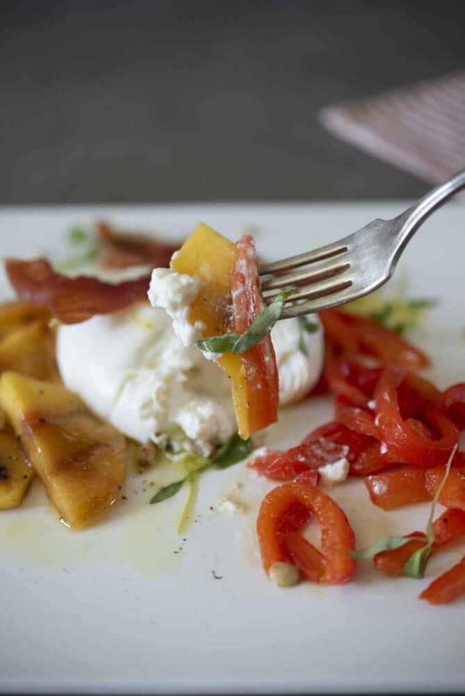 A fork with a bite of burrata, red pepper and peach