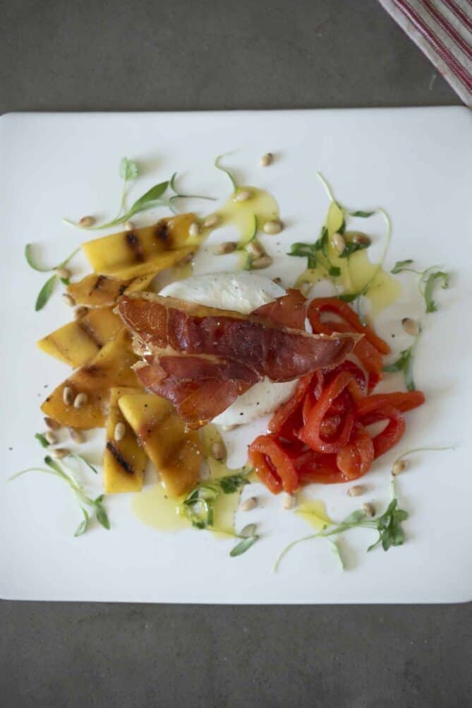 Strips of crispy prosciutto with slices peaches, red pepper and burrata cheese