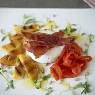 Creamy burrata surrounded by sliced peach, red pepper strips and prosciutto