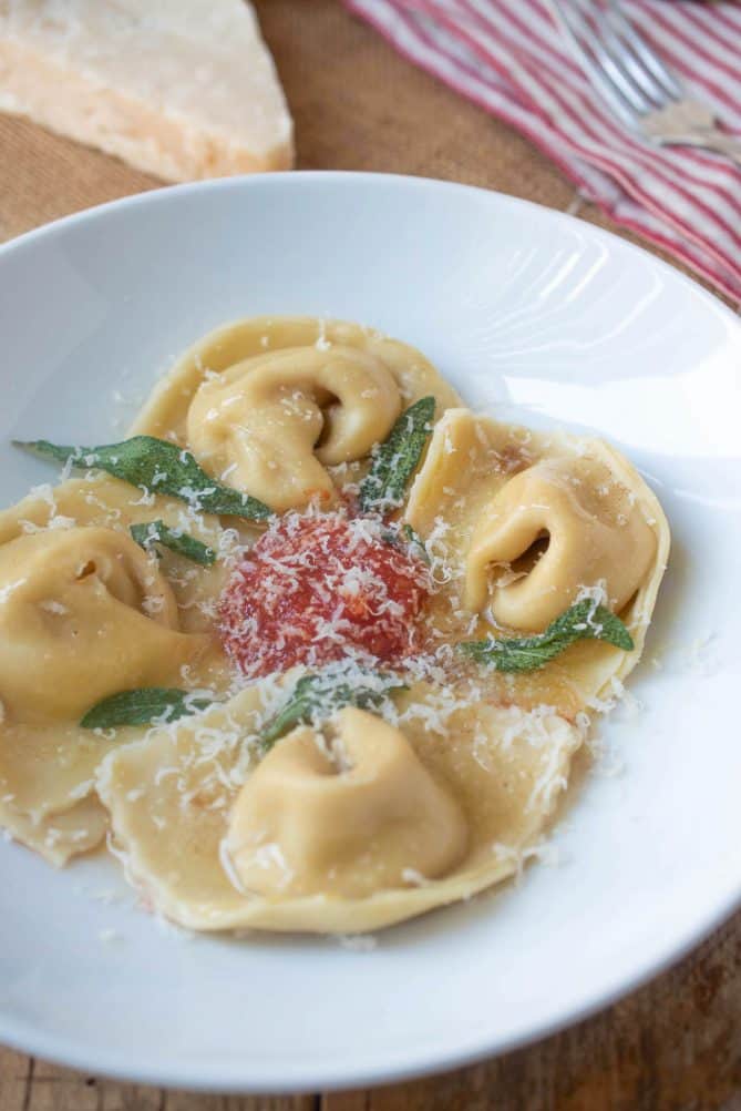 Fresh pasta folded into cappellacci shape to look like nuns hats with brown butter, crispy sage, red pasta sauce and grated Parmesan cheese