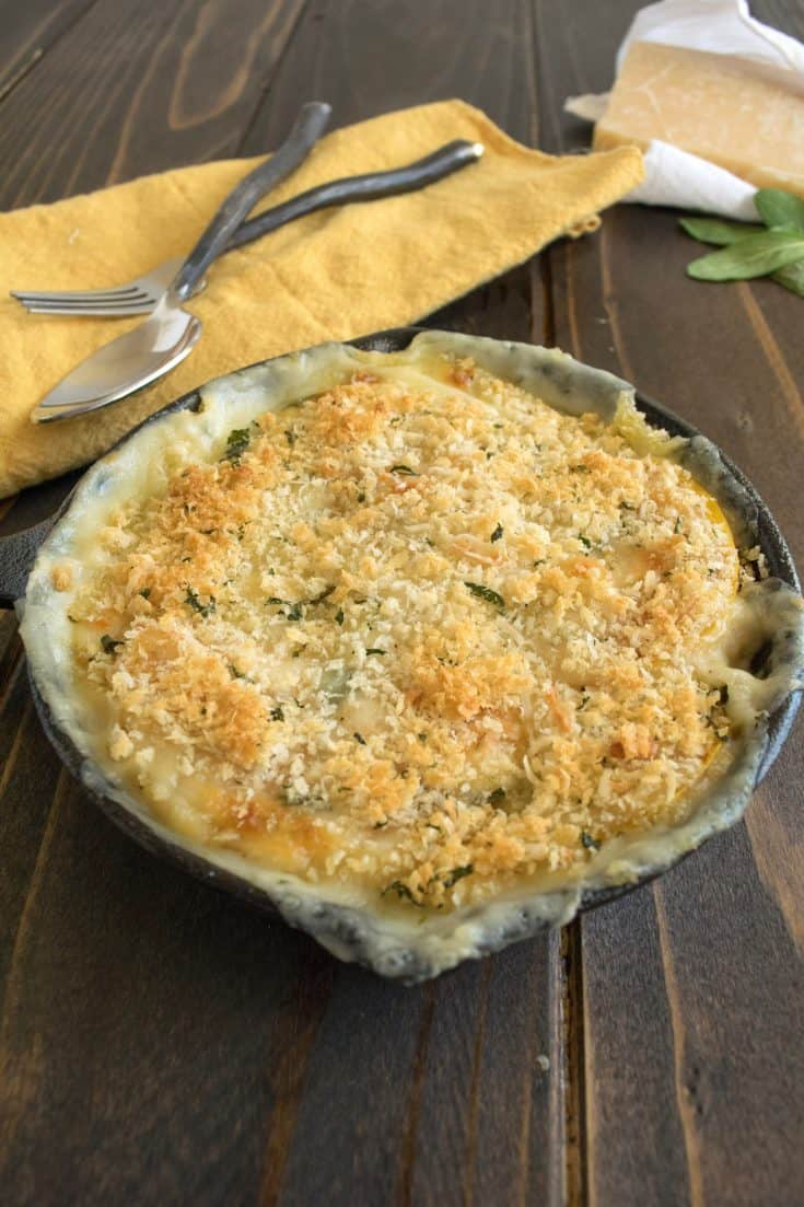A cast iron skillet of butternut squash and sage gratin with serving spoons