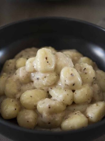 A black bowl filled with potato gnocchi in a cacio e pepe sauce