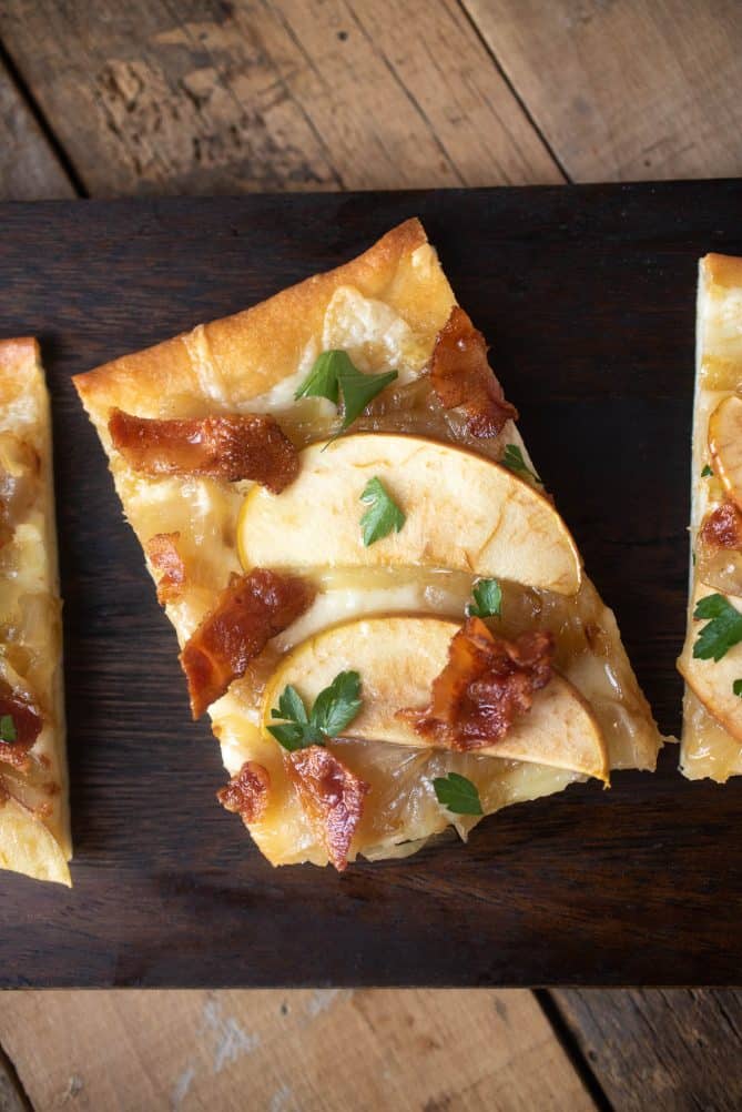 A rectangle shaped piece of flatbread with 2 apple slices, crispy bacon bits and chopped parsley