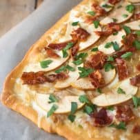 A closeup of the crispy brown edges of flatbread topped with melted fontina, caramelized onions apple slices and crispy bacon.