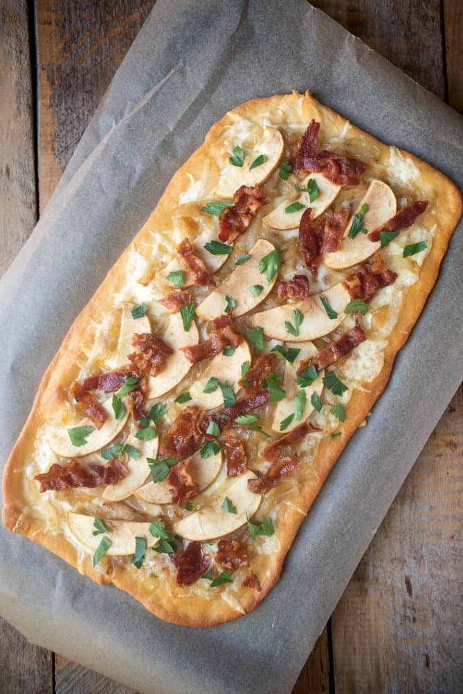 A caramelized onion apple and bacon flatbread pizza from overhead on a baking sheet shaped in a long rectangle