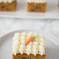 A slice of carrot cake square with decorative frosting on a white plate