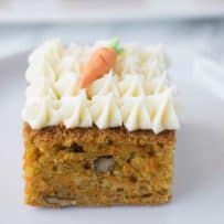 A square of carrot cake topped with cream cheese frosting and a decorative carrot