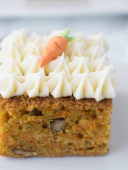 A square of carrot cake topped with cream cheese frosting and a decorative carrot