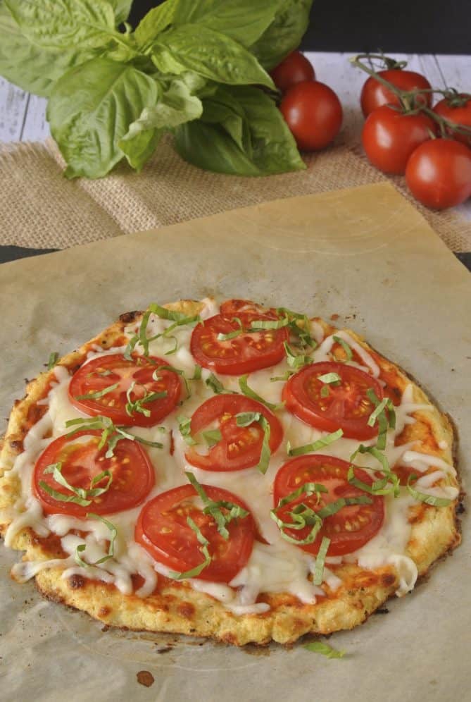 Slices of tomato and shredded basil on a cauliflower crust pizza