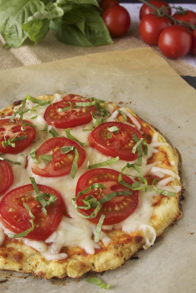 A closeup of cauliflower crust pizza showing the sweet tomato slices, melted cheese and basil toppings