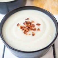 Creamy yet dairy free cauliflower and fennel soup in a black bowl topped with bacon crumbles