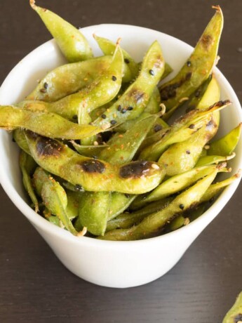Cooked edamame in a bowl topped with togarashi spice and black sesame seeds