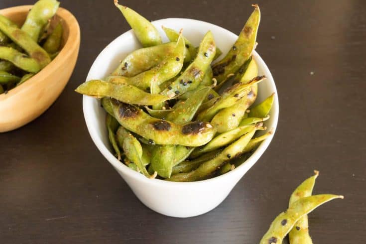 Cooked edamame in a bowl topped with togarashi spice and black sesame seeds