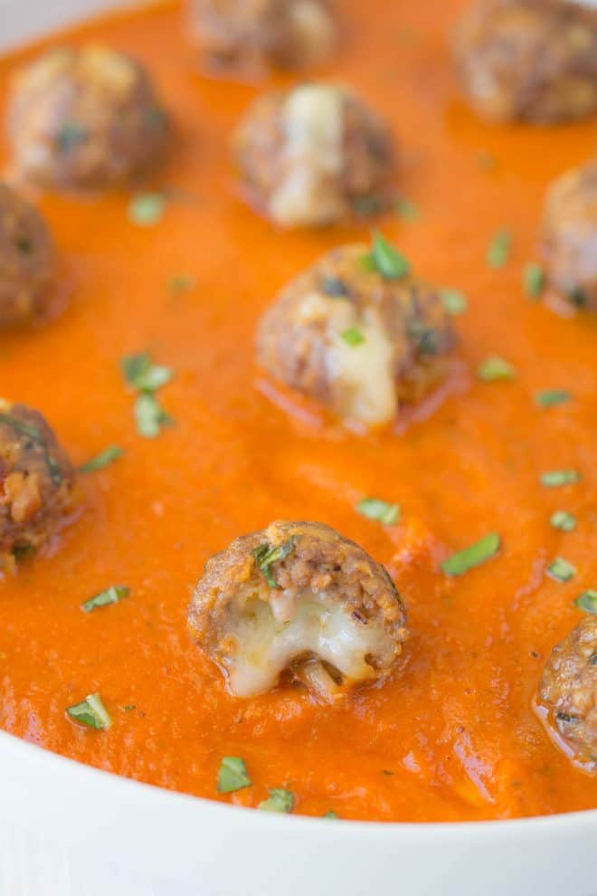 A mini meatball stuffed with melted cheese in tomato sauce sprinkled with chopped basil