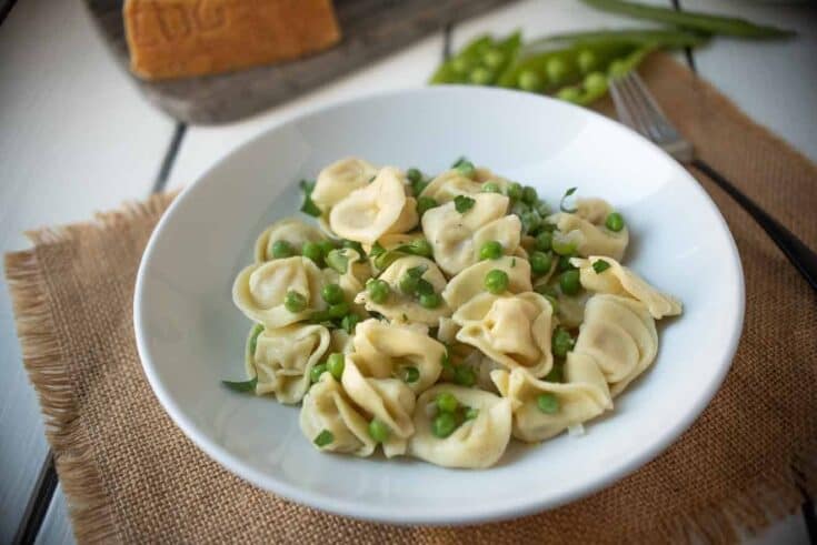 A white bowl with cheese tortellini with green peas