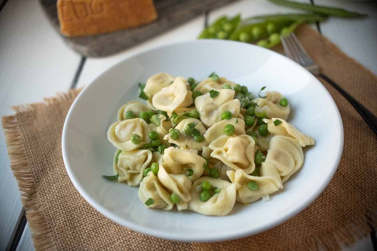 A white bowl with cheese tortellini with green peas