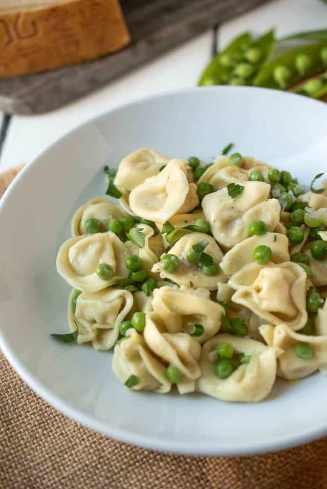 A closeup of tortellini topped with peas and chopped parsley