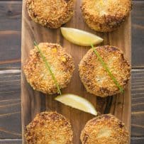 5 cheesy tuna melt cakes on a serving board with lemon wedges and chives