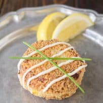 A cheesy tuna melt cake on a plate with a drizzle, chives and lemon