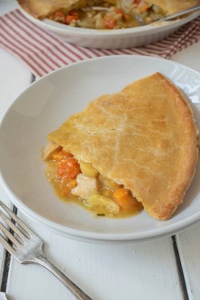 A slice of chicken pot pie with winter vegetables on a white plate