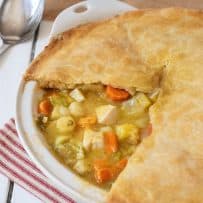 A chicken pot pie in a white dish with a slice removed showing the vegetables and chicken inside