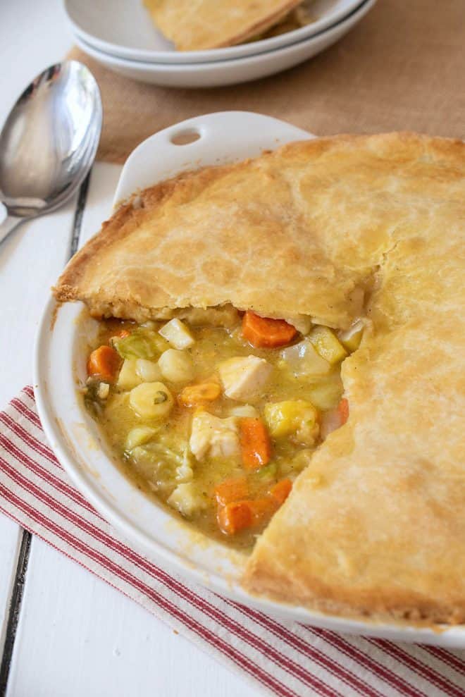 A chicken pot pie in a white dish with a slice removed showing the vegetables and chicken inside