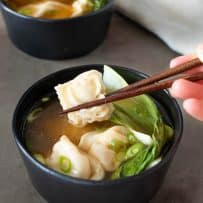 Holding a wonton with chopstick with a bowl of wonton soup