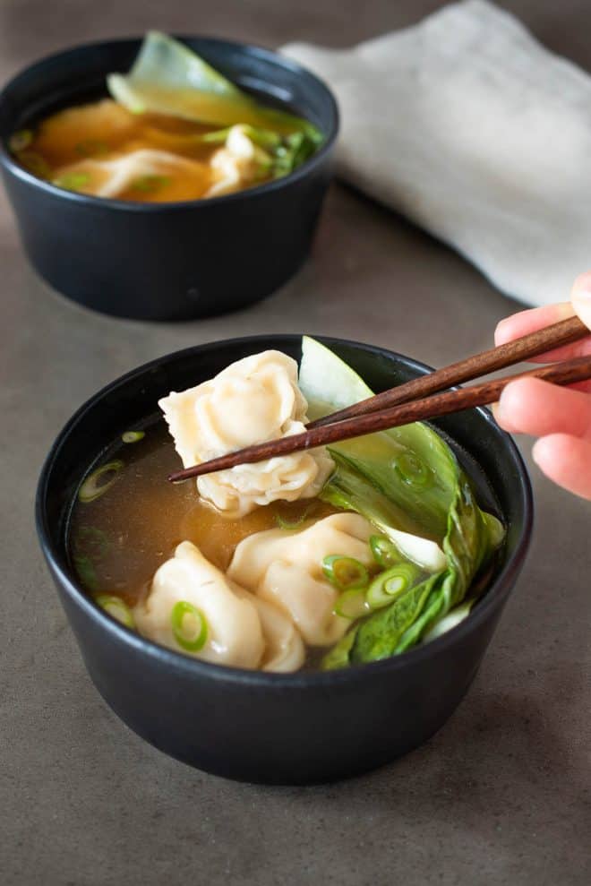 Holding a wonton with chopstick with a bowl of wonton soup