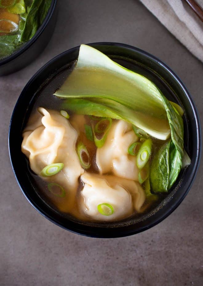 A black bowl with chicken wontons, bok choy and broth