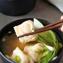 Holding a chicken wonton with chopsticks over a bowl of wonton soup
