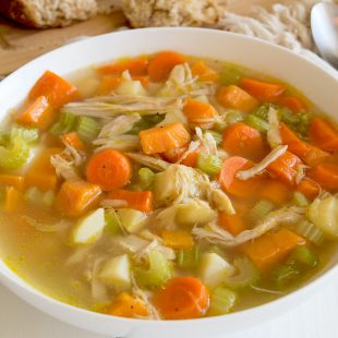 The best chicken soup served in a white bowl with a napkin, spoon and bread
