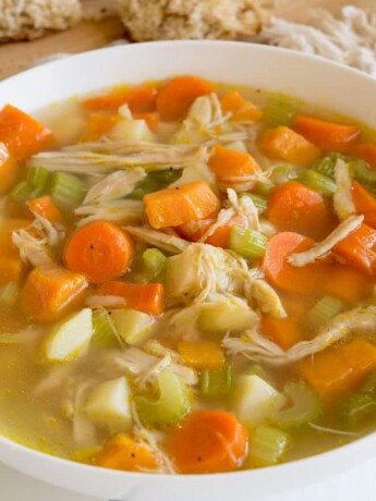 The best chicken soup served in a white bowl with a napkin, spoon and bread