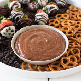 The dip in a white bowl with pretzels for dipping and chocolate covered strawberries