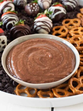 The dip in a white bowl with pretzels for dipping and chocolate covered strawberries