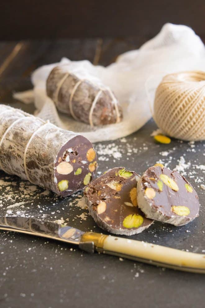 A chocolate salami with some slices on a slate board wrapped in string with a knife