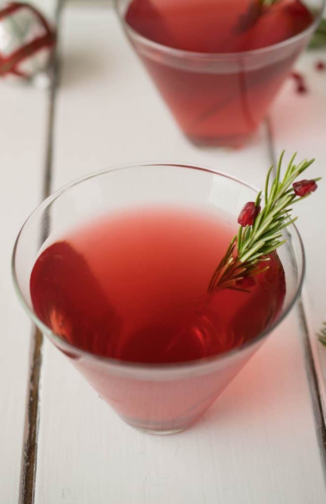 A ruby red drink garnished with fresh rosemary and pomegranate seeds
