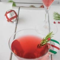 A Christmas Cosmopolitan in a short glass and one in a martini glass with holiday decorations