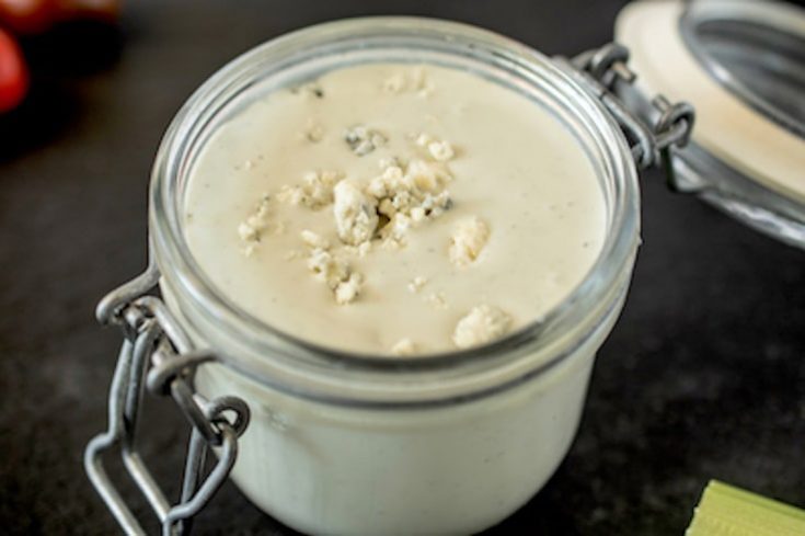A closeup of chunky blue cheese dressing in a jar showing the chunks of blue cheese