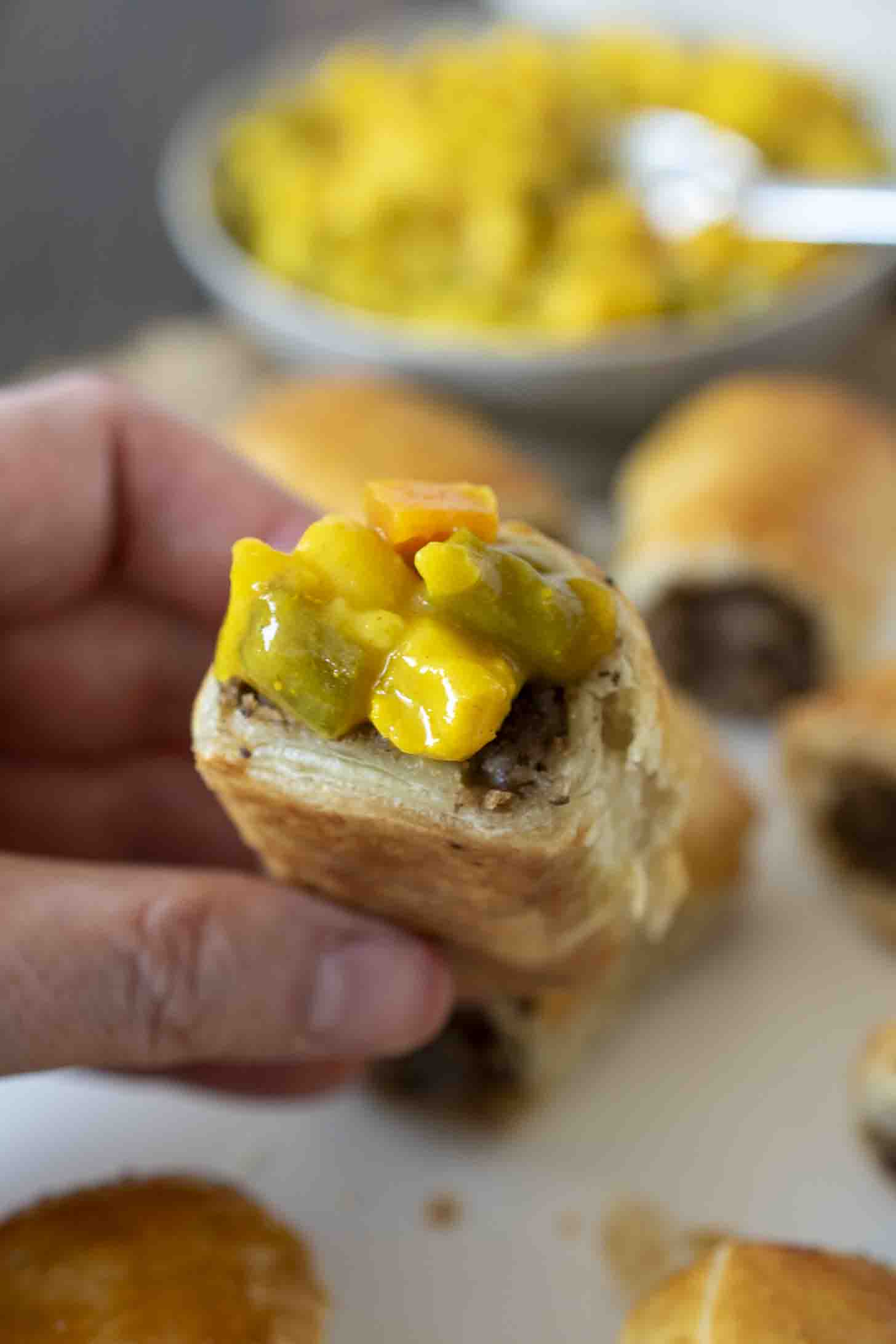 Holding a sausage roll topped with piccalilli relish