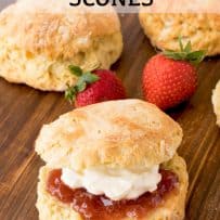 A scone cut in half and sandwiches with cream and jam with fresh strawberries behind